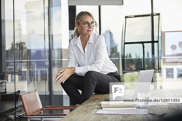Successful businesswoman sitting on desk  contemplating