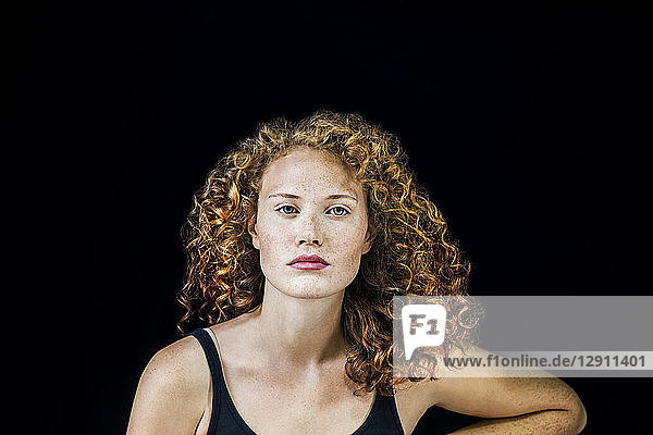 Portrait of freckled young woman with curly red hair in front of black background