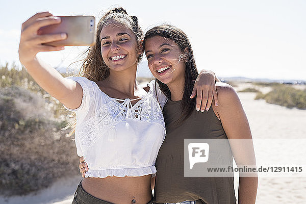 Girlfriends having fun on the beach  taking smartphone selfies