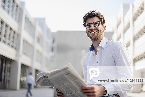 Smiling businessman sitting in the city reading newspaper