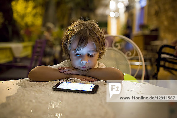 Boy sitting at table outdoors at night looking at smartphone