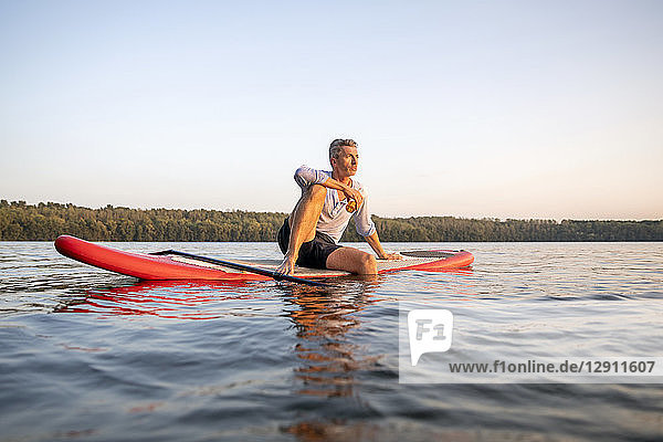 Man sitting on paddleboard on a lake by sunset relaxing