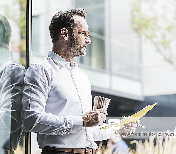 Businessman with papers and coffee to go looking at distance
