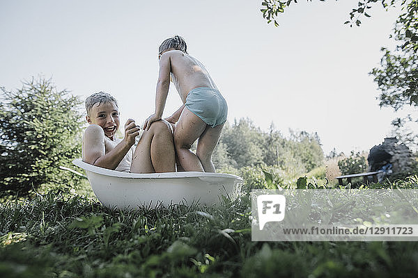 Brother and sister playing with water in little bath tub in garden