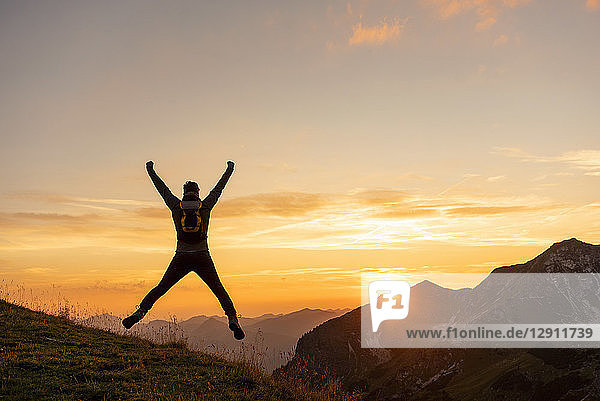 Germany  Bavaria  Oberstdorf  man on a hike in the mountains jumping at sunset