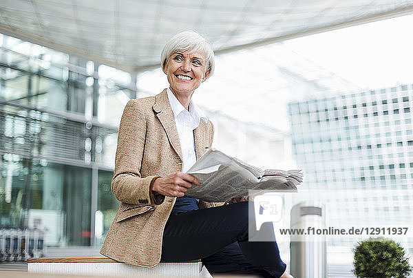 Smiling senior businesswoman sitting in the city with newspaper