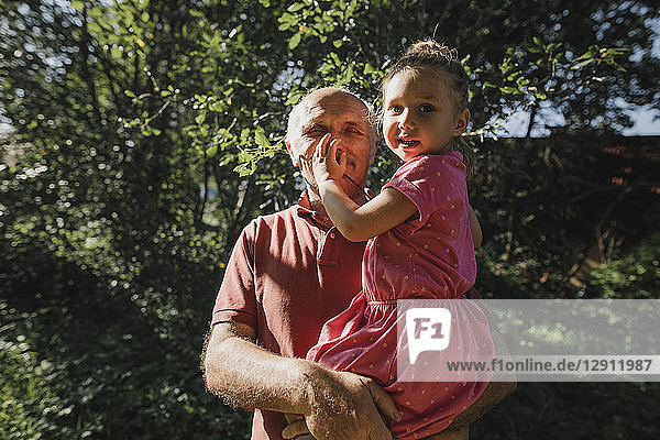 Grandfather carrying granddaughter in garden