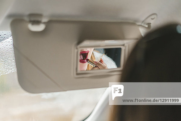 Woman mirrored in rear view mirror applying red lipstick in car