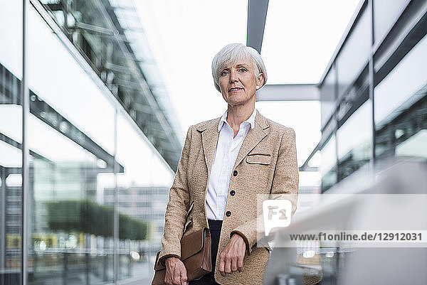 Portrait of confident senior businesswoman leaning on railing in the city