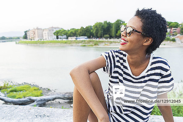 Smiling young woman wearing sunglasses sitting at the riverside