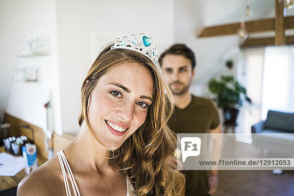 Portrait of smiling woman wearing tiara at home with man in background