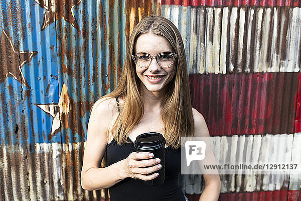Young woman holding cup of coffee  standing in front of metal fence with stars and stripes