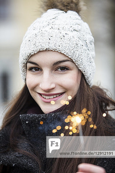 Portrait of smiling young woman with sparkler wearing bobble hat