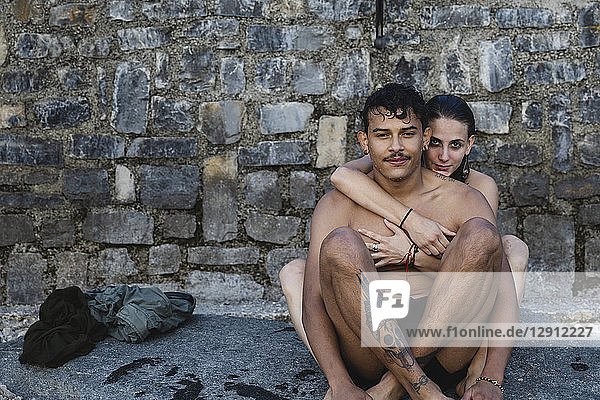 Portrait of affectionate young couple in swimwear sitting at a stone wall