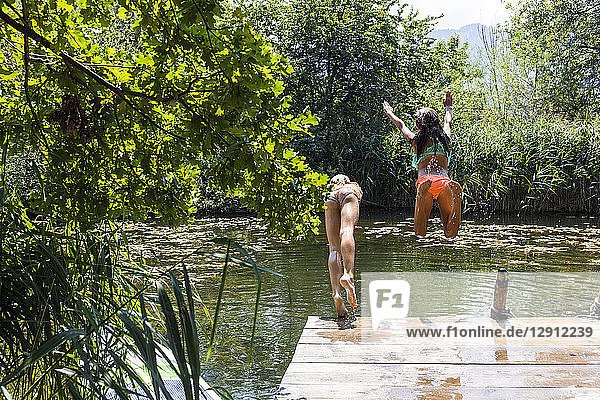 Two carefree girls jumping into pond