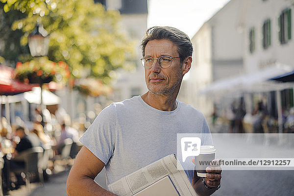 Mature man walking in he city with newspaper and digital tablet  drinking coffee