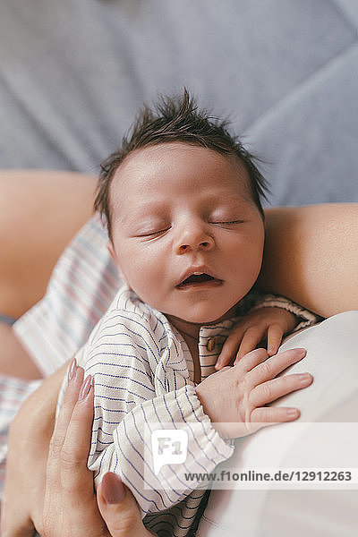 Portrait of newborn baby with closed eyes being held by mother