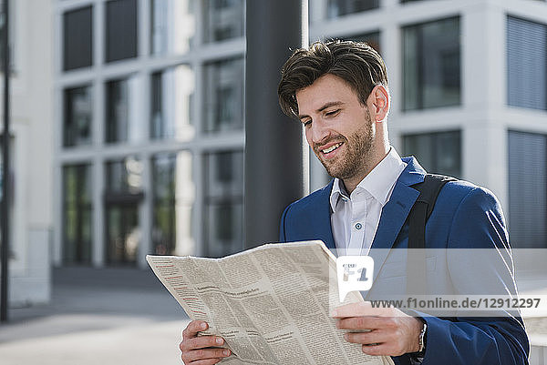 Smiling businessman reading newspaper in the city