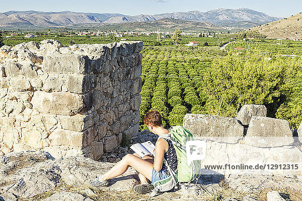 Greece  Peloponnese  Argolis  Tiryns  archaeological site  female tourist reading guide book