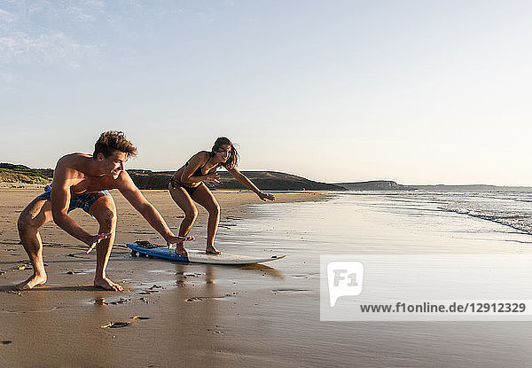 Young man showing young woman how to surf on the beach