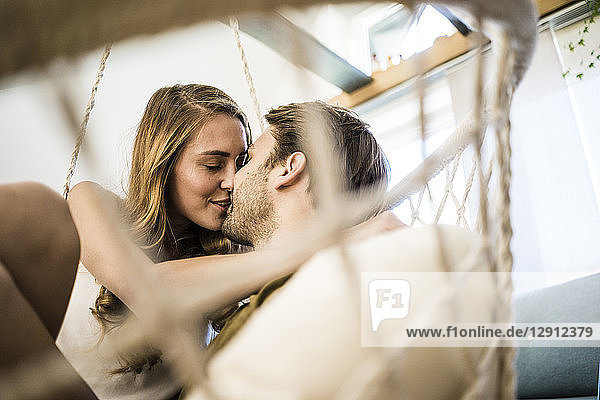 Happy affectionate couple kissing in hanging chair at home