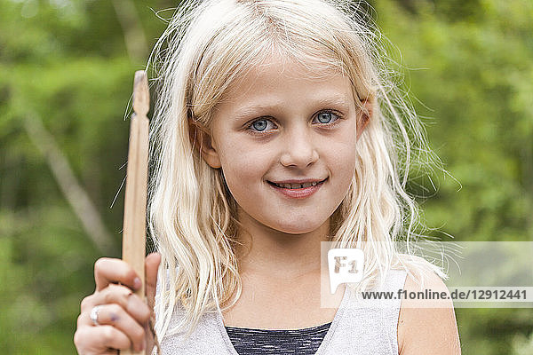 Portrait of smiling girl holding wooden stick outdoors