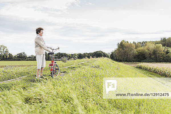 Senior woman with bicycle in rural landscape