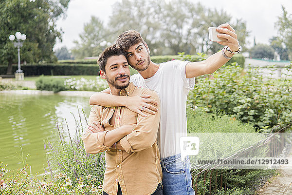 Portrait of young gay couple taking selfie with smartphone at city park