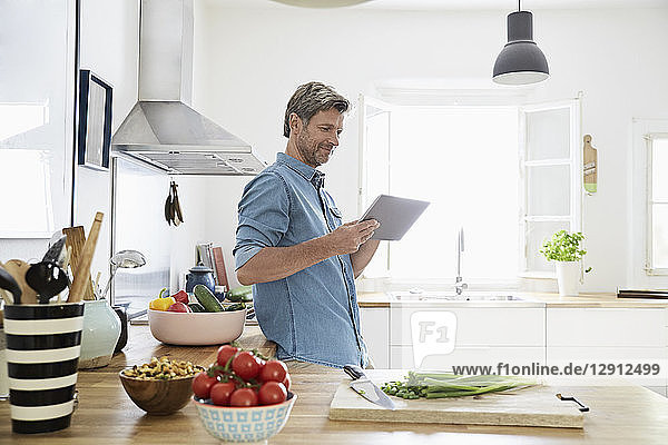 Mature man in his kitchen reading recipe on his digital tablet