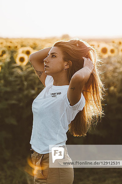 Portrait of a young woman standing in a field of sunflowers  hands in hair