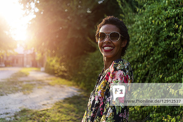 Portrait of happy young woman wearing sunglasses outdoors at sunset