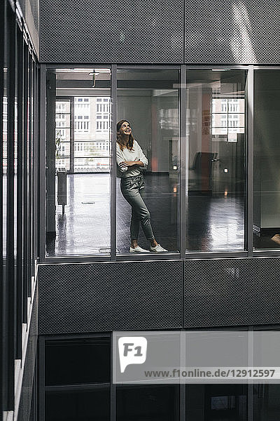 Woman standing at office window  looking up  smiling