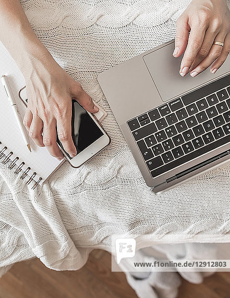 Woman working on bed with laptop and smartphone  partial view