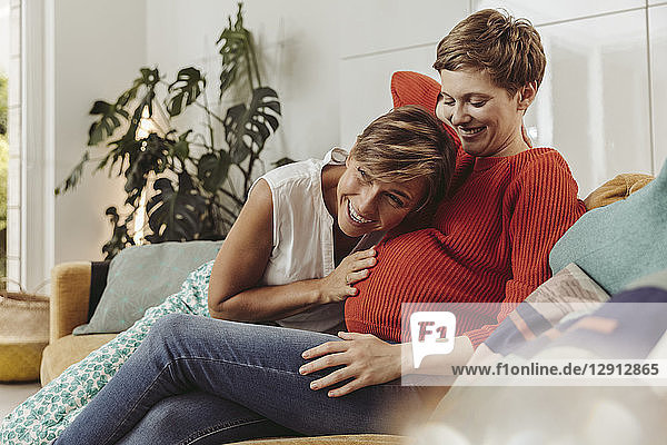 Happy lesbian couple feeling movements of baby belly of the expectant mother