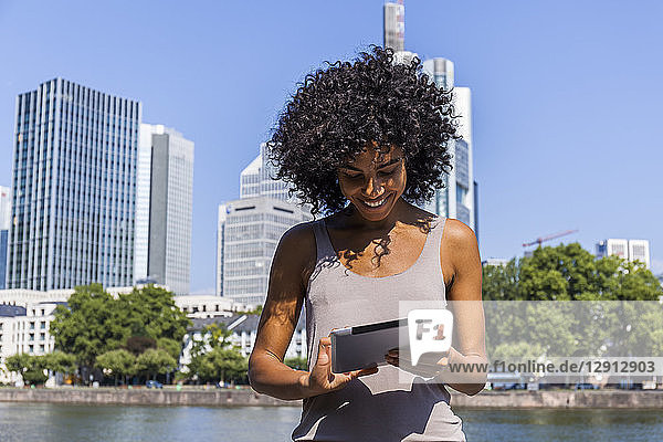 Germany  Frankfurt  smiling young woman with curly hair using tablet in the city