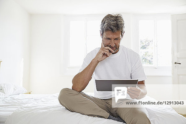 Portrait of mature man with digital tablet in bedroom