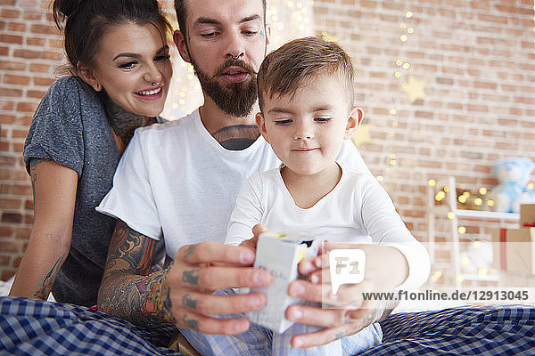 Boy opening Christmas present with parents in bed