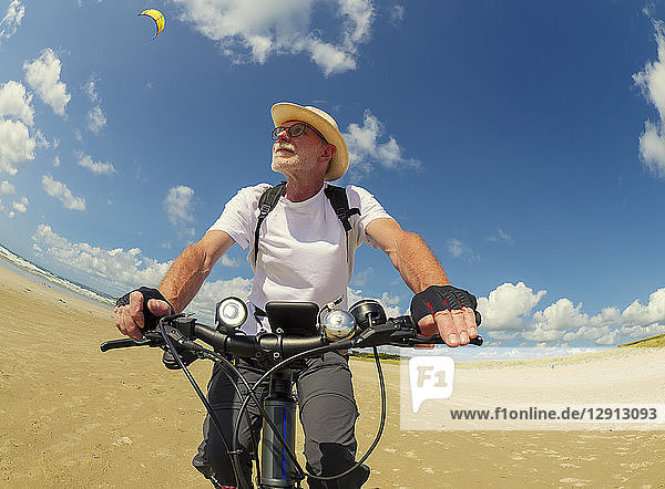 France  Bretagne  Sainte-Anne la Palud  Plage de Treguer  senior man riding mountain e-bike on beach