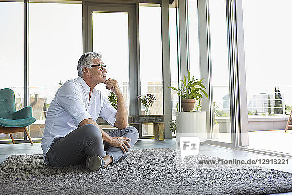 Pensive mature man sitting on carpet at home