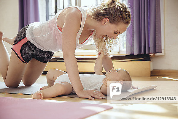 Mother playing with her baby on yoga mat while working out