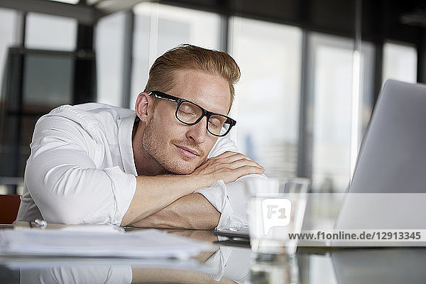 Businessman leaning on desk in office with closed eyes