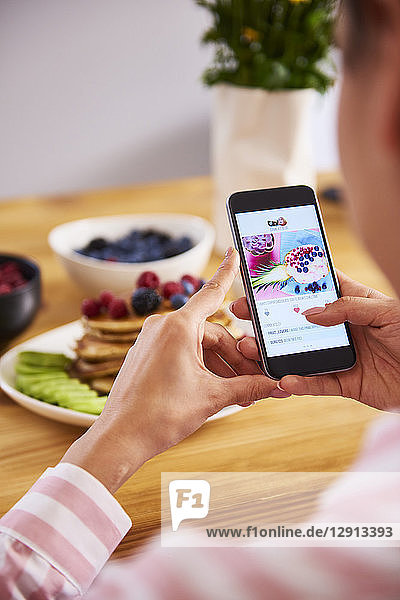 Young woman taking pictures of breakfast pancakes with berries and fresh fruit