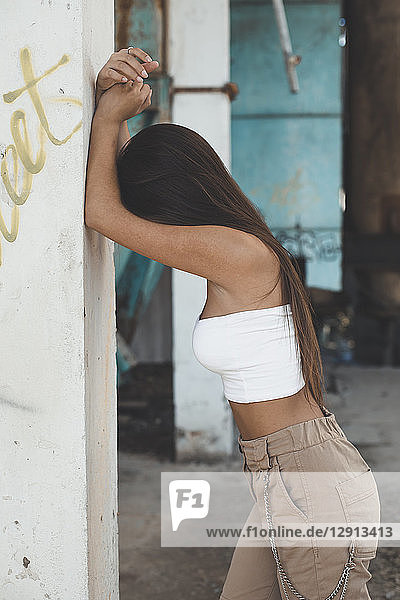 Fashionable teenage girl with long brown hair leaning against wall