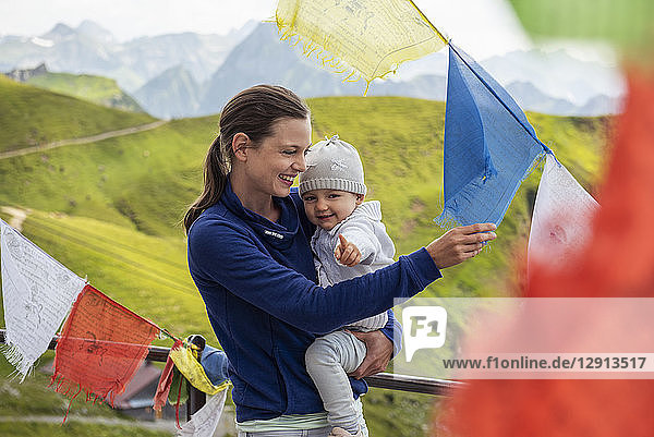 Germany  Bavaria  Oberstdorf  happy mother carrying little daughter on a mountain hut surrounded by pennants