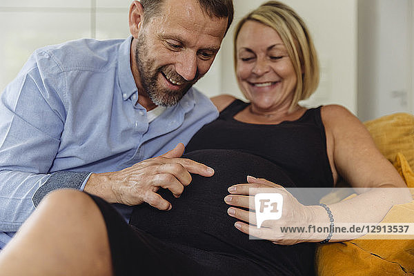 Mature man and his pregnant mature wife sitting on couch touching her belly
