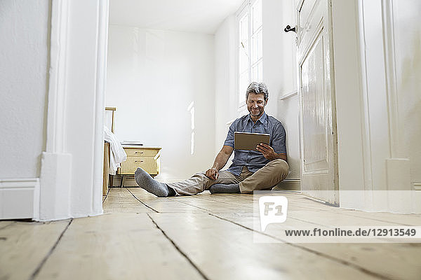 Marture man sitting on floor of his bedrom  using digital tablet