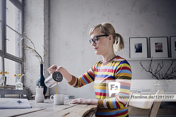 Woman pouring coffee in a mug at desk in a loft