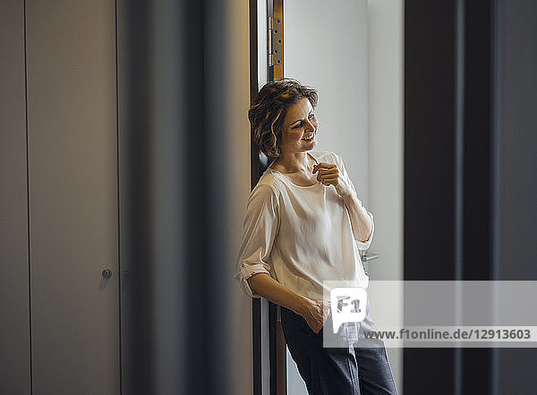 Businesswoman leaning relaxed in door frame of her office