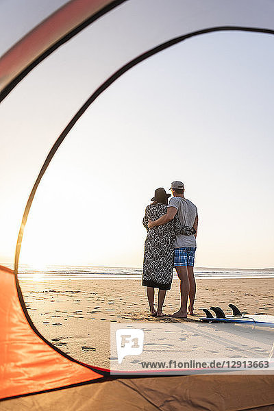 Romantic couple camping on the beach  embracing at sunset