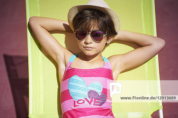 Young girl wearing swimwear  sunglasses and a sun hat  sitting in sun lounger